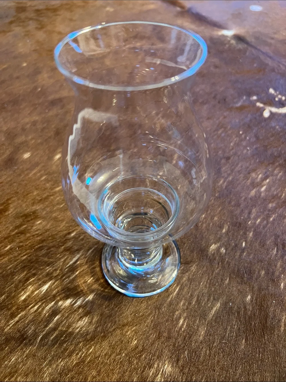 Clear glass hurricane candle holder features a pedestal base and a flared top